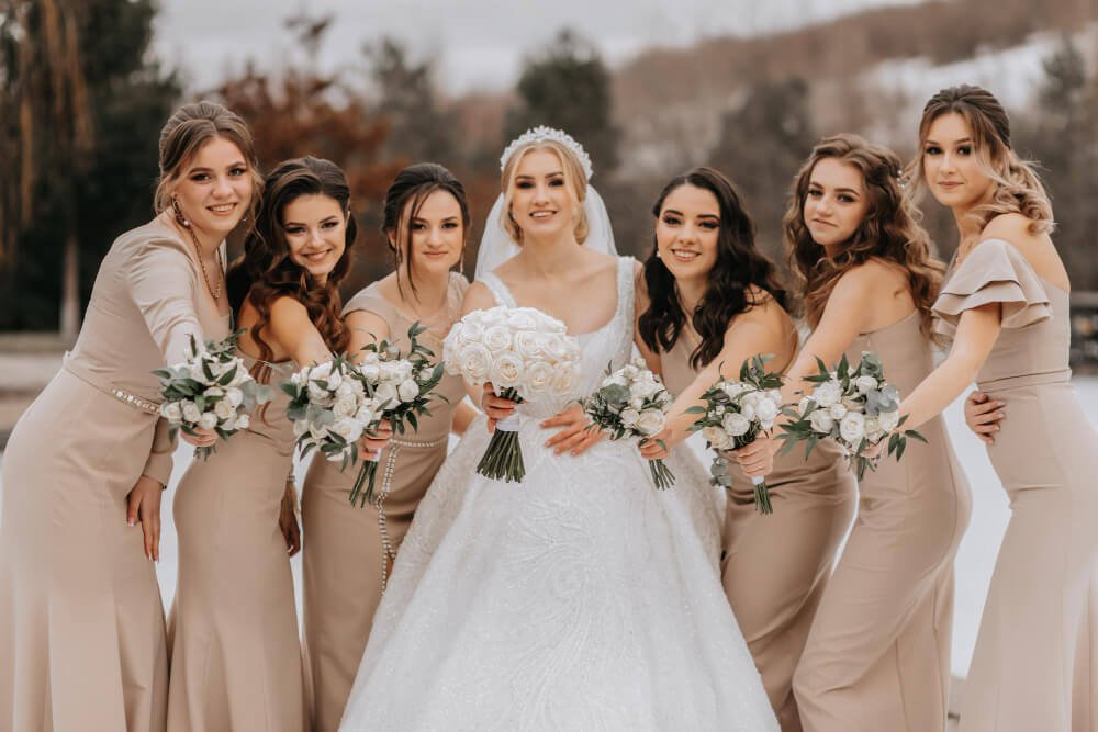 The bride and her bridesmaids pose holding bouquets and looking at the bride Winter wedding